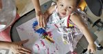 standing with AADC | AADC News | Rylae-Ann has physical therapy while in her stander, by painting with her hands on a colorful sheet of paper, with the assistance of one of her parents
