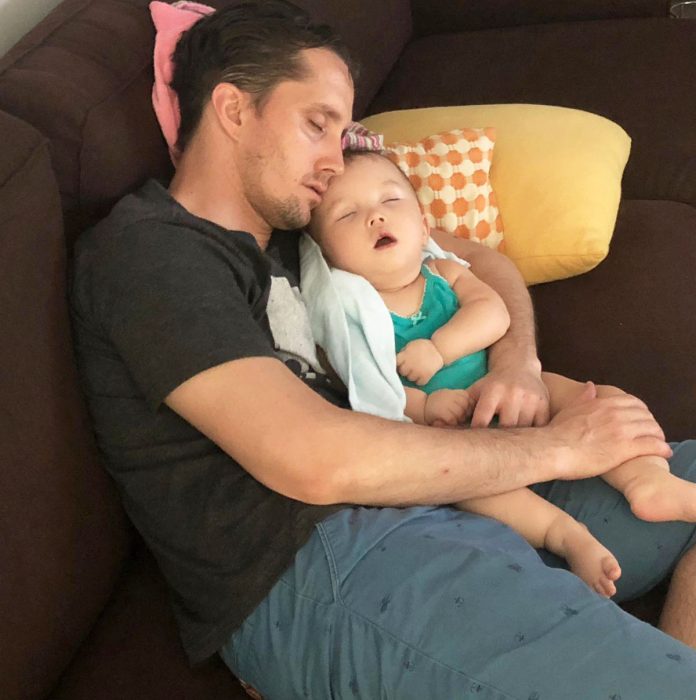 AADC News | Dad sleeps while holding Rylae-Ann upright on the couch