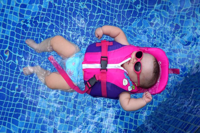 water therapy | AADC News | Rylae-Ann floats on her back in the pool, wearing a pink and purple life vest and pink sunglasses.