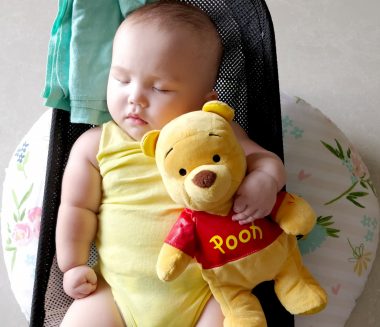 awareness for AADC deficiency | AADC News | Rylae-Ann sleeps in a yellow onesie, holding tight to a Winnie the Pooh plush figure