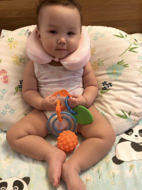 AADC symptoms | AADC News | Rylae-Ann is supported by a neck pillow and a boppy pillow due to her weak neck muscles. She is holding a toy in her hands. 