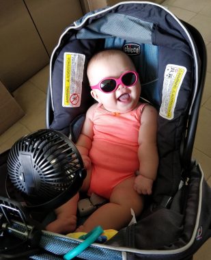 AADC symptoms | AADC News | A fan blows on Rylae-Ann to help her with her excessive sweating. She is sitting in a carrier and wearing pink sunglasses.