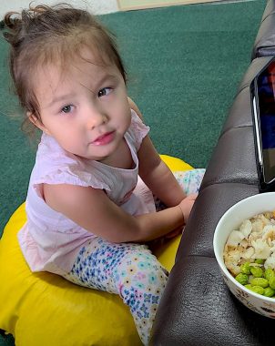 | AADC News | Rylae-Ann sits on a yellow cushion and looks to her right with a cute expression as a bowl of fish and soybean meal sits on the table in front of her