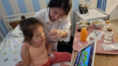 AADC News | Rylae-Ann eats her first meal in the hospital after hip surgery. She's watching an animated TV show on a tablet.