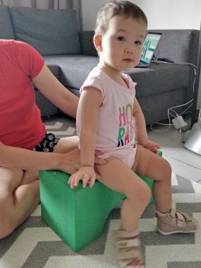 exercises | AADC News | Rylae-Ann sitting on a block without back support, save her mom's hands at her hips. Rylae-Ann's feet are on the floor.
