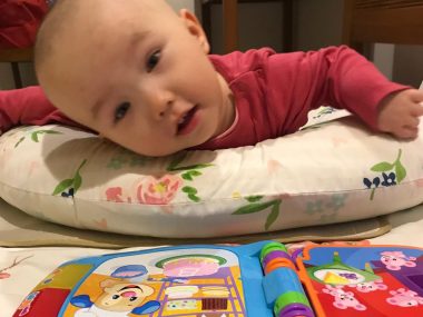 exercises | AADC News | Rylae-Ann, lying on her tummy on a pillow, with a book in front of her