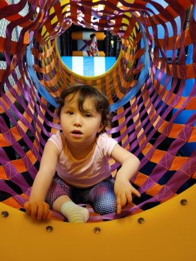 AADC deficiency | AADC News | Rylae-Ann emerges from a colorful mesh tube that is part of an indoor playground.