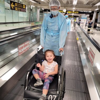 children with special needs | AADC News | photo of Rylae-Ann in a wheelchair on a moving sidewalk, with an airport porter behind her