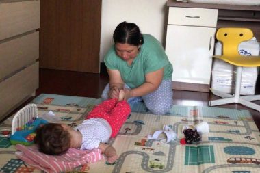 massage for children | AADC News | Rylae-Ann's nanny massages her feet while Rylae-Ann lies on the floor surrounded by toys.