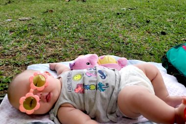 hypoglycemic crisis | AADC News | Rylae-Ann when she was a baby, lying on a blanket on the grass in the park. She's wearing funky orange and yellow sunglasseslies