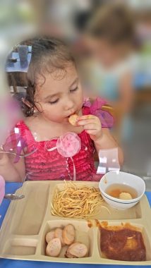 oral placement therapy | AADC News | Rylae-Ann wears a red and pink dress and eats her lunch from from a tray