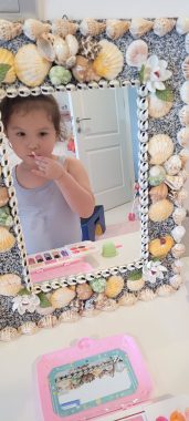 walking at night | AADC News | Rylae-Ann applies makeup while standing in front of a mirror framed by seashells.
