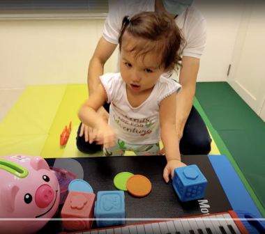 benefits of music therapy | AADC News | A young Rylae-Ann stands in front of a table of toys, including blocks and a small piano.