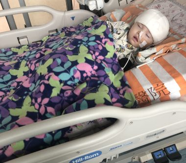 caregiver self-care | AADC News | A young Rylae-Ann recovers in a hospital bed. Her head is wrapped in bandages and she is hooked up to medical equipment