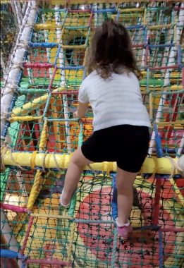 negative comments | AADC News | Rylae-Ann climbs a multicolored rope wall at an indoor playground.