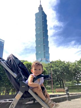 negative comments | AADC News | Rylae-Ann sits in her stroller at the park and smiles at the camera. Taipei 101 is featured in the background.