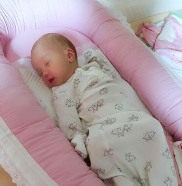 A newborn baby girl sleeps in a pink cocoon-style bed. 