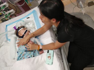 A woman holds a baby on a bed in an intensive care unit.