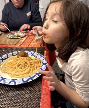A young girl eats spaghetti.