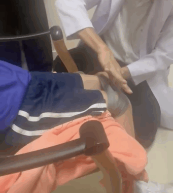 A physical therapist kneels next to a young child to assist her with leg exercises.