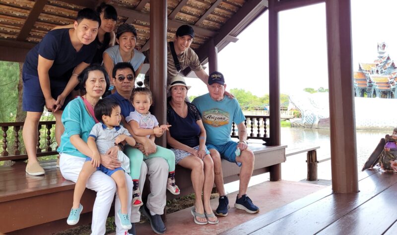Several generations of family pose for a photo. Some are seated on a wooden platform while others are standing behind them.