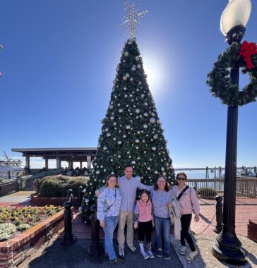 A group of people stand outdoors in front of a Christmas tree.