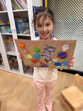 A young girl proudly holds up a 2-D model of the solar system that she created.