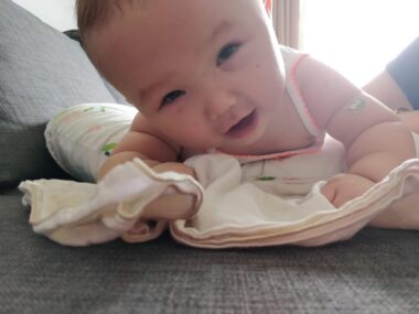 A young baby looks up as she lies on her stomach on the floor.