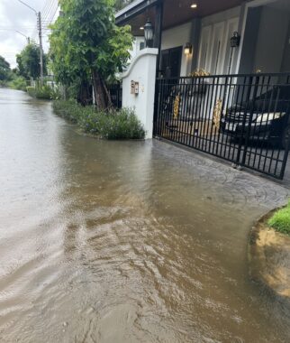 Floodwaters lap against the side of a house as a car sits behind a gate.